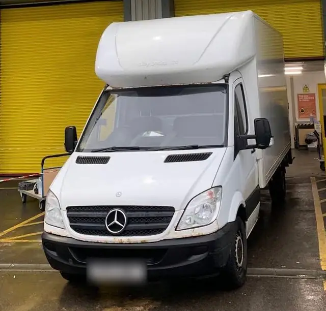 Front of a white Mercedes Luton van parked at a loading bay with yellow roller shutters behind it