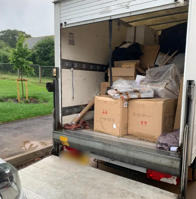 Back of a white Luton removal van with the tail lift down, loaded with boxes, bags and furniture on a house move